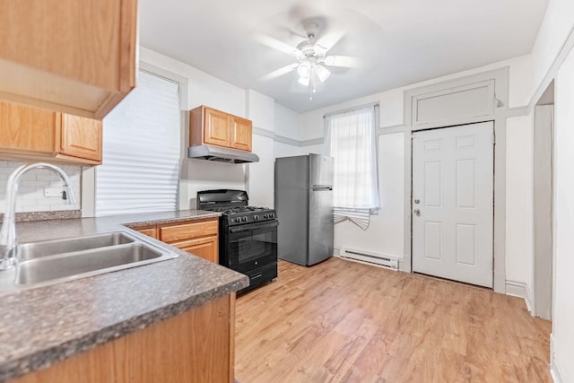 kitchen with under cabinet range hood, a baseboard heating unit, a sink, black range with gas stovetop, and freestanding refrigerator