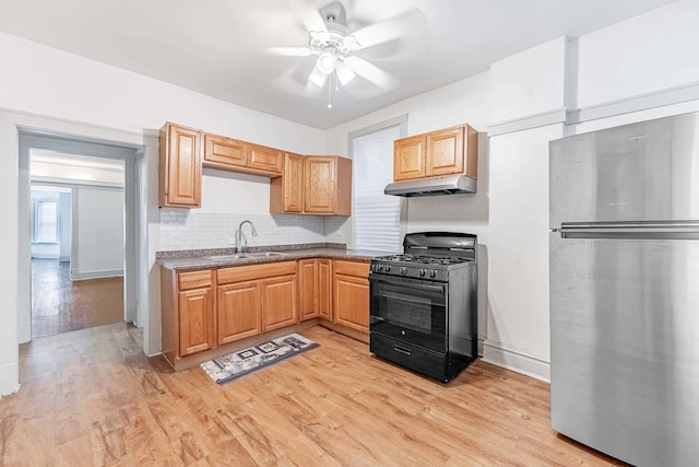 kitchen featuring black gas range, light wood-style floors, freestanding refrigerator, a sink, and under cabinet range hood