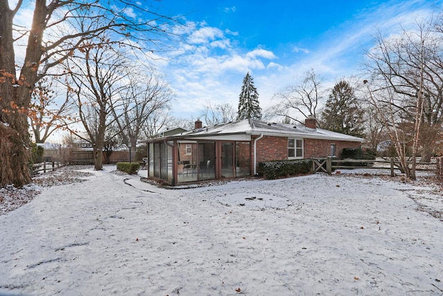 snow covered back of property with a sunroom, a chimney, fence, and brick siding