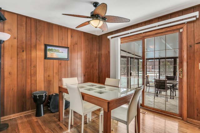 dining room featuring wood walls, wood finished floors, a ceiling fan, and baseboards