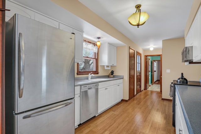 kitchen featuring stainless steel appliances, light wood-style flooring, white cabinetry, a sink, and baseboards