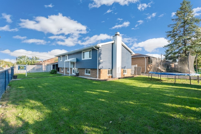 back of property with a fenced backyard, a trampoline, a chimney, and a lawn