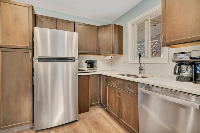 kitchen with stainless steel appliances, a sink, light countertops, light wood-type flooring, and tasteful backsplash