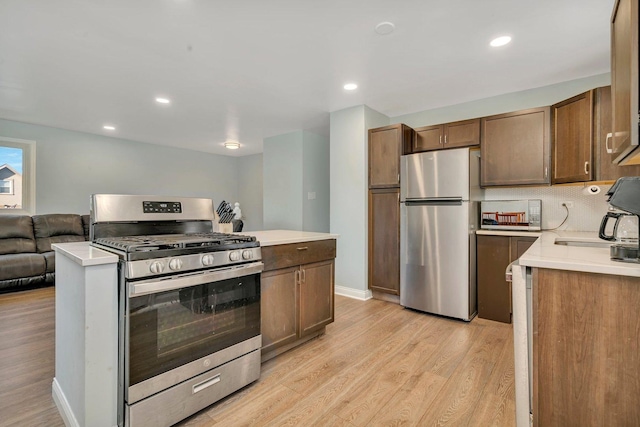 kitchen featuring decorative backsplash, open floor plan, stainless steel appliances, light countertops, and light wood-style floors