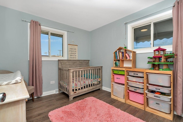 bedroom featuring a nursery area, baseboards, and wood finished floors