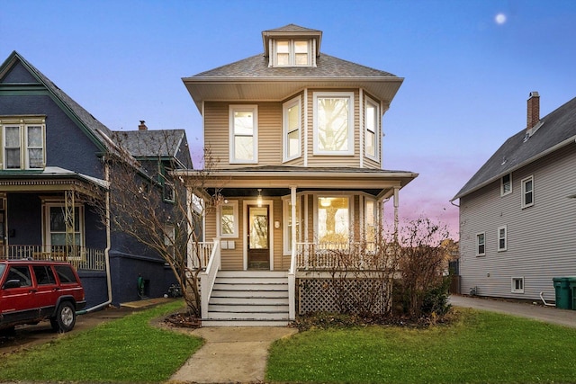 american foursquare style home with a lawn, a porch, and roof with shingles