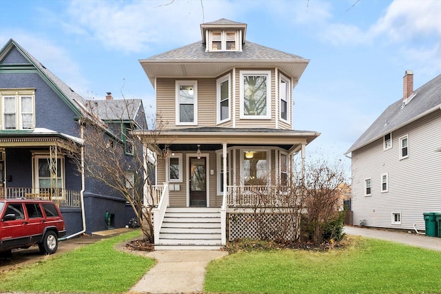 american foursquare style home featuring covered porch, a shingled roof, and a front lawn