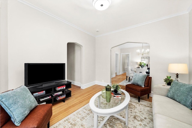 living area featuring a notable chandelier, ornamental molding, wood finished floors, arched walkways, and baseboards