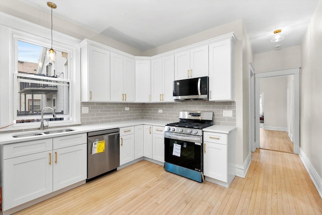 kitchen featuring light wood-style flooring, a sink, stainless steel appliances, light countertops, and tasteful backsplash