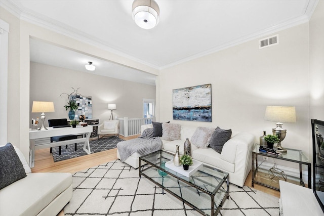 living area featuring baseboards, wood finished floors, visible vents, and ornamental molding