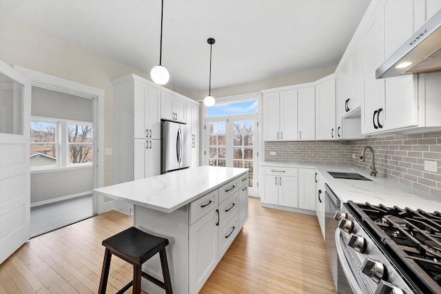 kitchen with under cabinet range hood, stainless steel appliances, tasteful backsplash, and a sink