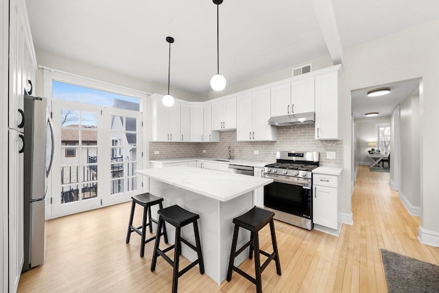 kitchen featuring under cabinet range hood, appliances with stainless steel finishes, a kitchen breakfast bar, light wood-type flooring, and backsplash