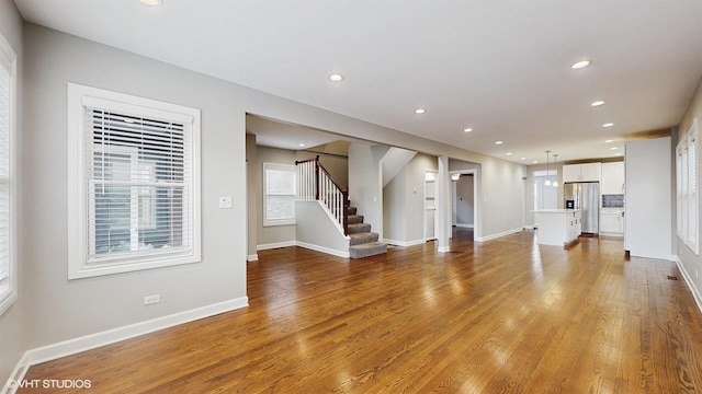 unfurnished living room with stairway, wood finished floors, and baseboards