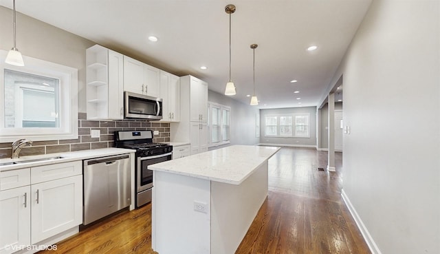 kitchen with backsplash, a kitchen island, appliances with stainless steel finishes, wood finished floors, and a sink