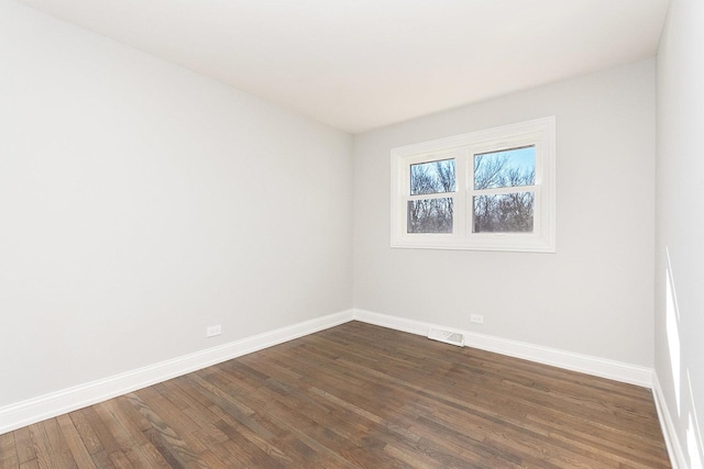 empty room with dark wood-type flooring, visible vents, and baseboards