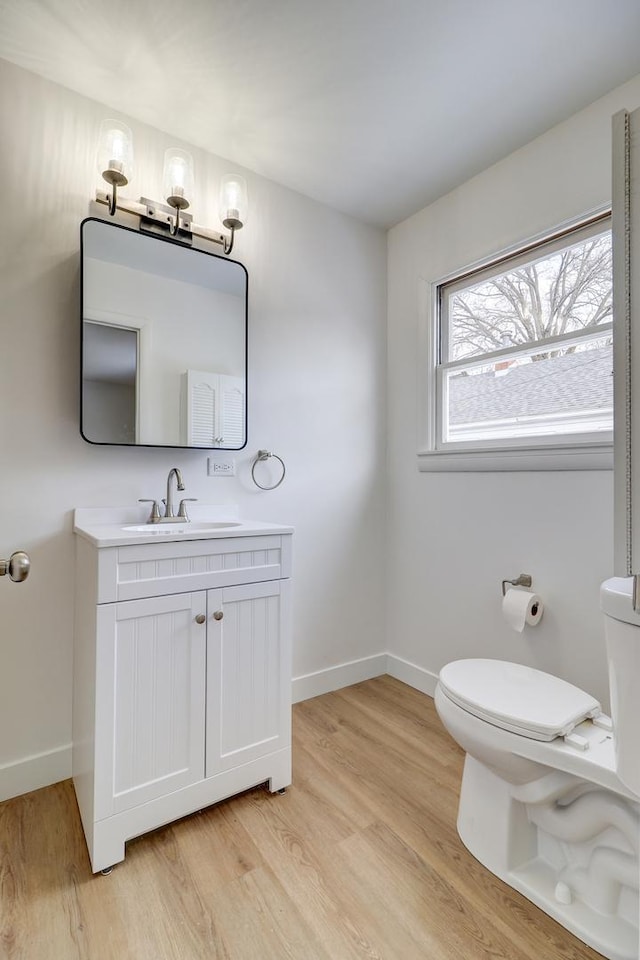 half bathroom featuring toilet, baseboards, wood finished floors, and vanity