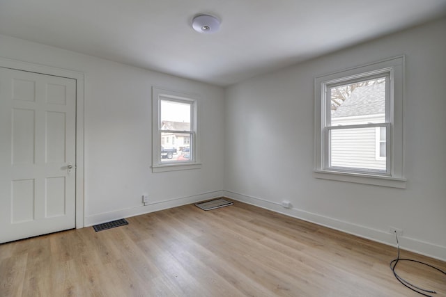 spare room with light wood-type flooring, visible vents, and baseboards