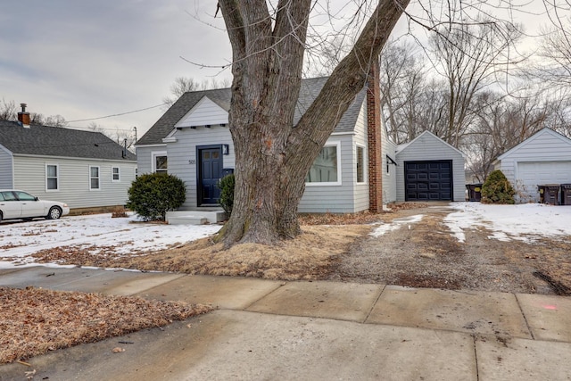 view of front of home with a shingled roof, a detached garage, and an outbuilding