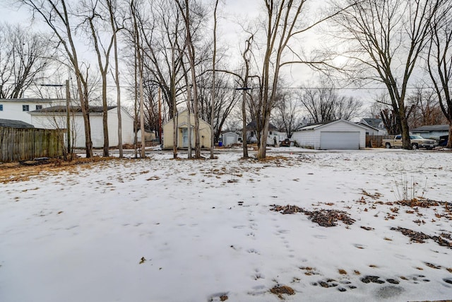 snowy yard featuring a detached garage, fence, and an outdoor structure