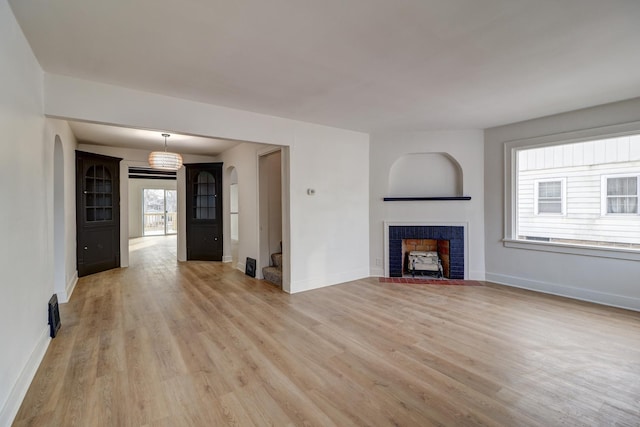 unfurnished living room featuring arched walkways, a tile fireplace, light wood-type flooring, baseboards, and stairs