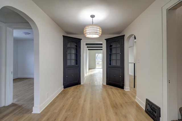 entrance foyer featuring light wood-style floors, baseboards, visible vents, and arched walkways