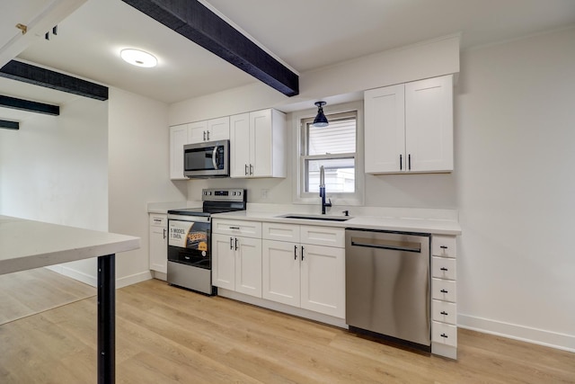 kitchen featuring light wood finished floors, stainless steel appliances, white cabinets, a sink, and beamed ceiling