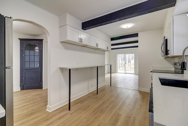 kitchen with arched walkways, stainless steel appliances, white cabinets, light wood-type flooring, and beamed ceiling