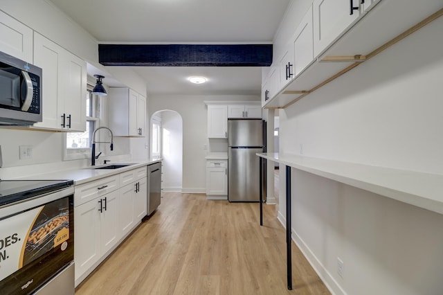 kitchen with light wood finished floors, arched walkways, white cabinets, appliances with stainless steel finishes, and a sink