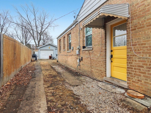 view of side of property featuring brick siding, a detached garage, fence, an outdoor structure, and concrete driveway