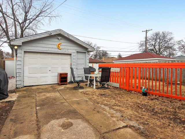 detached garage featuring concrete driveway and fence