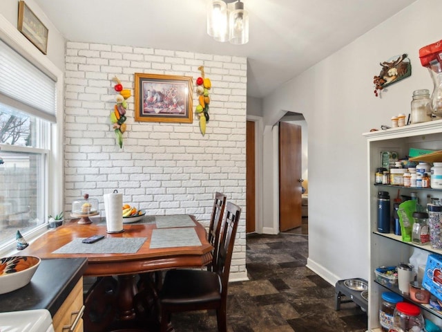 dining area featuring arched walkways, baseboards, and brick wall