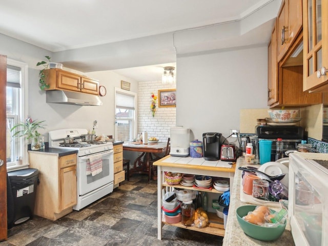 kitchen featuring open shelves, tile counters, stone finish floor, white range with gas cooktop, and under cabinet range hood