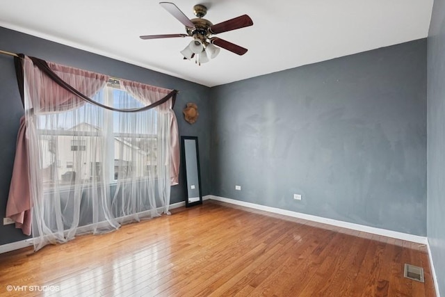 empty room featuring ceiling fan, hardwood / wood-style flooring, visible vents, and baseboards