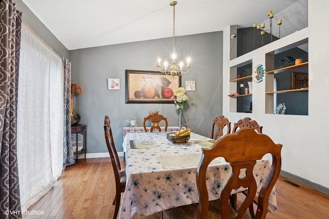 dining space with baseboards, visible vents, lofted ceiling, hardwood / wood-style floors, and an inviting chandelier