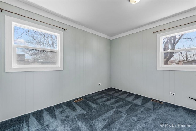 empty room featuring visible vents, a healthy amount of sunlight, and dark carpet