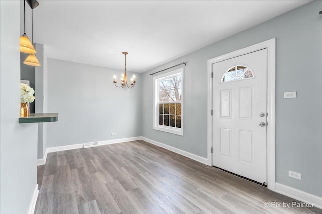 foyer entrance featuring visible vents, baseboards, a notable chandelier, and wood finished floors