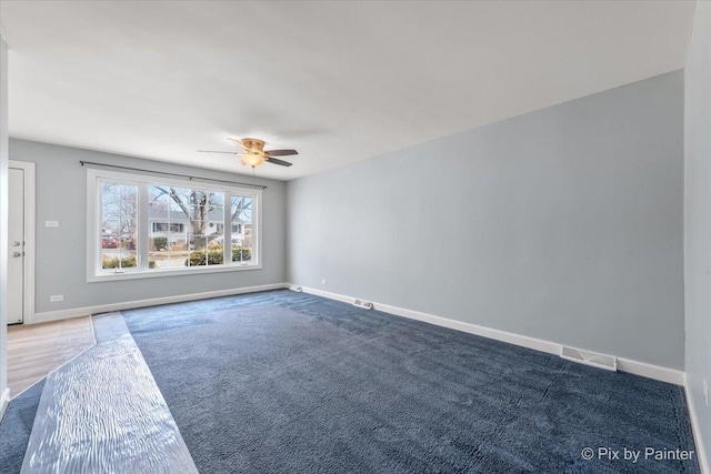 carpeted spare room featuring baseboards, visible vents, and ceiling fan