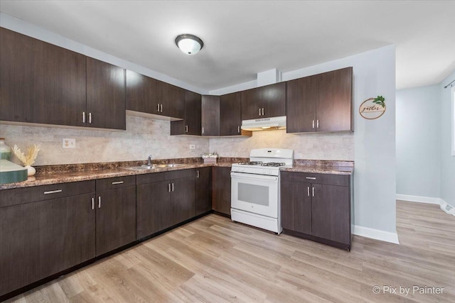 kitchen with white gas stove, a sink, light wood-style floors, under cabinet range hood, and backsplash