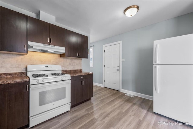 kitchen featuring white appliances, dark countertops, under cabinet range hood, and dark brown cabinetry