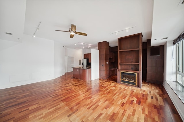 unfurnished living room with a glass covered fireplace, rail lighting, visible vents, and light wood finished floors