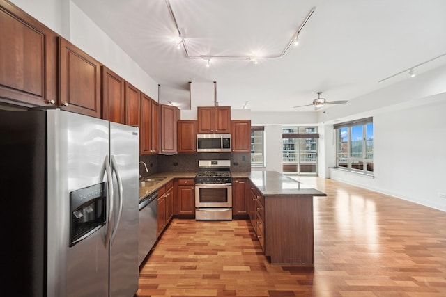 kitchen with stone countertops, decorative backsplash, appliances with stainless steel finishes, a peninsula, and light wood-style floors