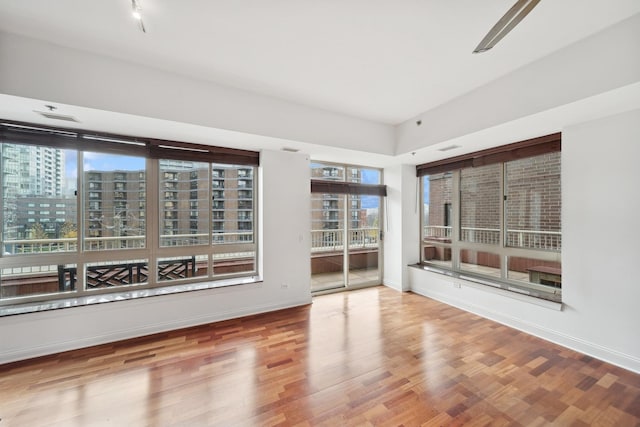 unfurnished room with a view of city, baseboards, and wood finished floors