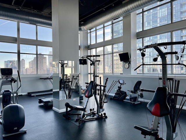 workout area with a view of city, plenty of natural light, a towering ceiling, and baseboards