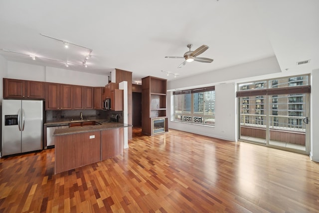 kitchen with stainless steel appliances, dark countertops, open floor plan, a sink, and wood finished floors