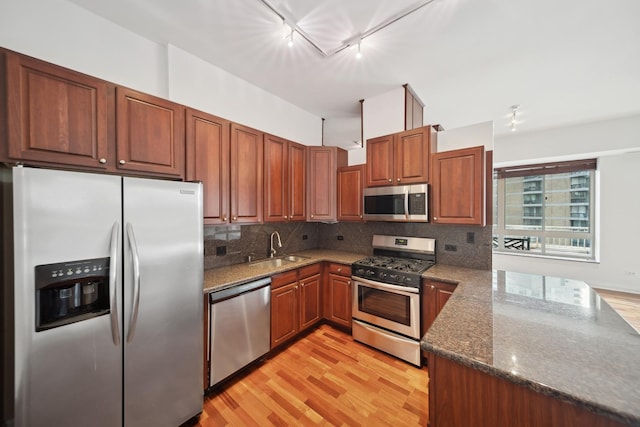 kitchen with stainless steel appliances, decorative backsplash, light wood-style floors, a sink, and dark stone countertops