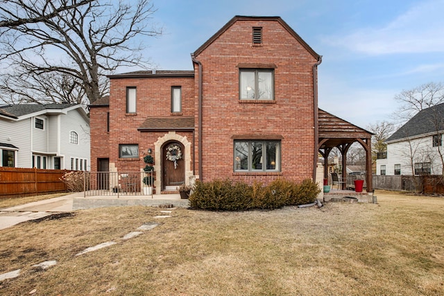 view of front facade featuring brick siding, fence, a front lawn, and a patio