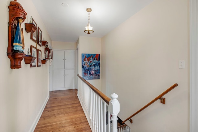 hallway with baseboards, an upstairs landing, and light wood-style floors