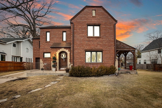 view of front facade featuring a patio area, brick siding, a lawn, and fence