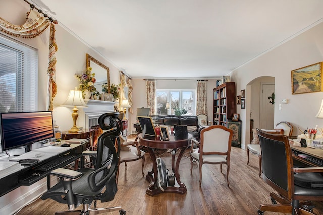 office featuring ornamental molding, arched walkways, a fireplace, and wood finished floors