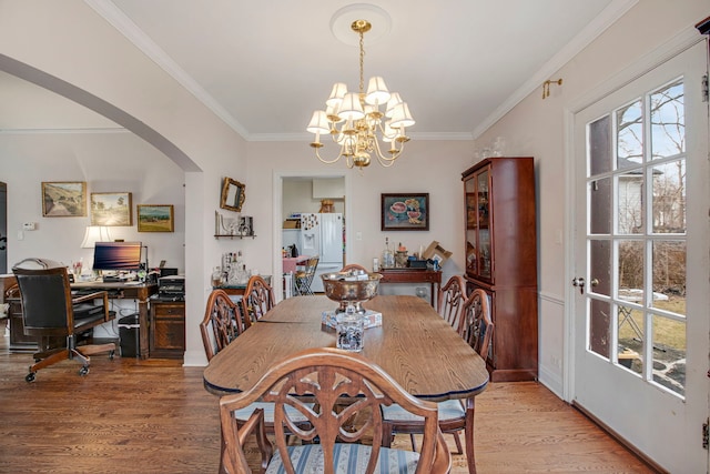 dining area with a chandelier, arched walkways, crown molding, and wood finished floors